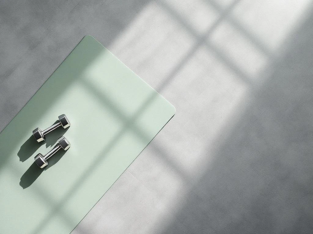 Bovenaanzicht van een yogamat, chromen dumbbells en weerstandsband op een schone gymvloer voor beginners