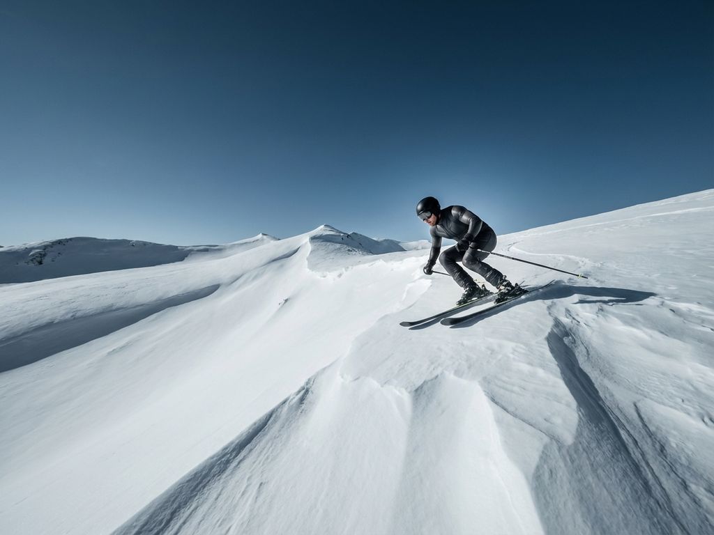 Skiër in perfecte houding glijdt elegant over witte helling tegen heldere blauwe lucht, toont kracht en uithoudingsvermogen