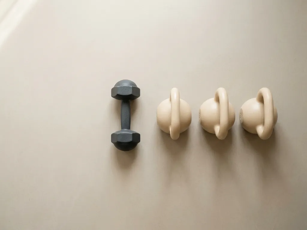Dumbbell en rij kettlebells op licht betonnen ondergrond, minimalistisch bovenaanzicht met zacht natuurlijk licht.